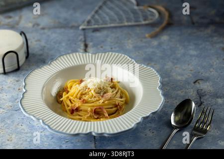 Cremige Spaghetti Carbonara serviert in einer dekorativen weißen Schüssel auf blauem Hintergrund Stockfoto