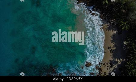 Hochwinkelansicht des tropischen Einlasses mit untergetauchten Felsen, weißer Surf und üppiger grüner Vegetation Stockfoto