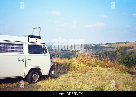 Sonniger Tagesblick auf Novi Sad von Fruška Gora mit einem weißen VW T2 Wohnmobil im Vordergrund, aufgenommen in warmen analogen 35-mm-Tönen. Stockfoto