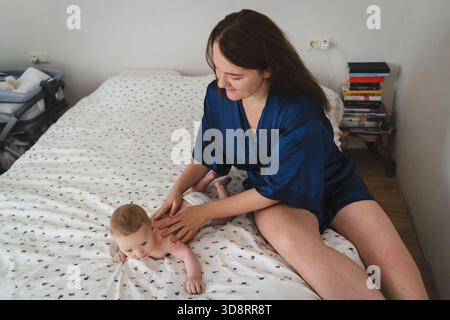 Mutter spielt mit ihrem Baby in einem gemütlichen Zimmer während der Morgenstunden auf dem Bett und genießt wertvolle Zeit miteinander Stockfoto