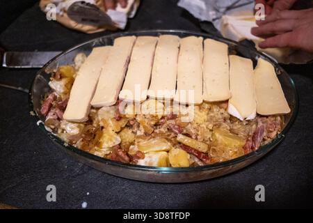 Nahaufnahme der Hände, die Tartlette mit Kartoffelschichten, Spachteln und Käse in einer Auflaufform in Cranves-Sales in Haute-Savoie in Auvergne-Rhone vorbereiten Stockfoto