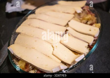 Nahaufnahme der Hände, die Tartlette mit Kartoffelschichten, Spachteln und Käse in einer Auflaufform in Cranves-Sales in Haute-Savoie in Auvergne-Rhone vorbereiten Stockfoto