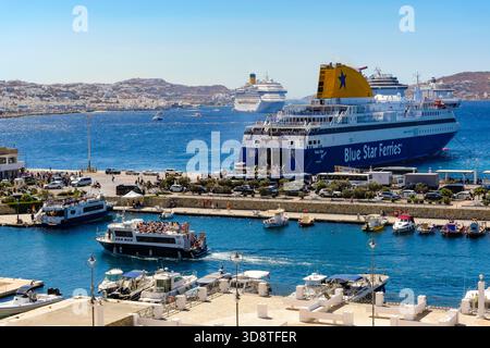 Mykonos, Kykladen, Griechenland - Mykonos New Port, eine Blue Star Ferries Fähre liegt am Kai im neuen Hafen vor der Skyline von Mykonos Town. Stockfoto