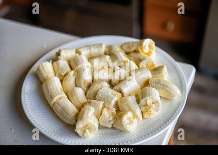 Bananen schneiden Stücke auf weißem Teller, Haufen von rohen, ungekochten geschälten Früchten zu Hause Küchentisch Theke Makronaht Stockfoto