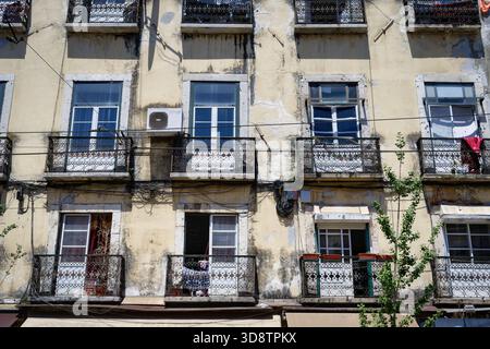 Detaillierte Ansicht Einer typischen, sonnenverwöhnten, baufälligen gelben Fassade in Lissabon mit alten weißen Fenstern, verzierten schwarzen schmiedeeisernen Balkonen und Power Li Stockfoto