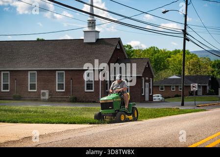 Lyndhurst, USA - 2. Mai 2025: Mann mittleren Alters, der auf dem John Deere Rasenmäher in Virginia unterwegs ist und im Sommer Gras an der Kirche mäht Stockfoto
