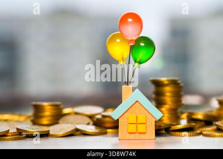 Farbenfrohes Ballonhaus, das den Traum symbolisiert, ein Haus zu besitzen, umgeben von Stapel goldener Münzen Stockfoto