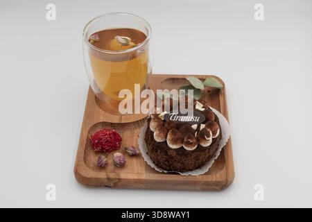 Tiramisu-Dessert mit Kräutertee auf Holztablett mit getrockneten Blumen und Eukalyptusblättern auf einem sauberen weißen Hintergrund Stockfoto