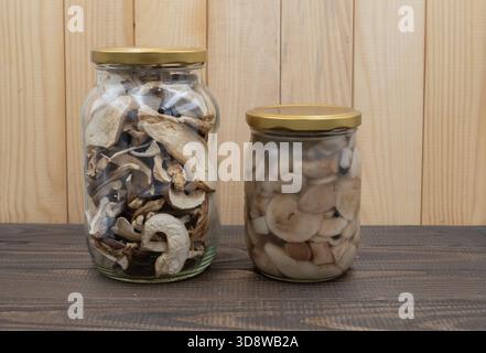 Getrocknete Stachelpilze und marinierte Pilze in Gläsern mit losen Scheiben auf rustikalem Holztisch Stockfoto