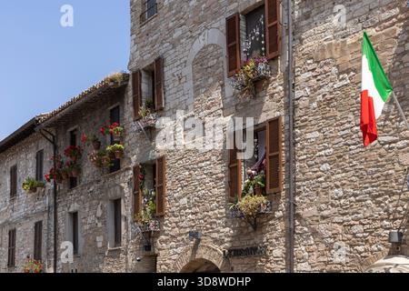 Assisi, Italien - 12. Juni 2025: Bezaubernde Fassaden von typischen mittelalterlichen Steinhäusern, Blumentöpfe. Holzläden schützen vor südlicher Sonne Stockfoto
