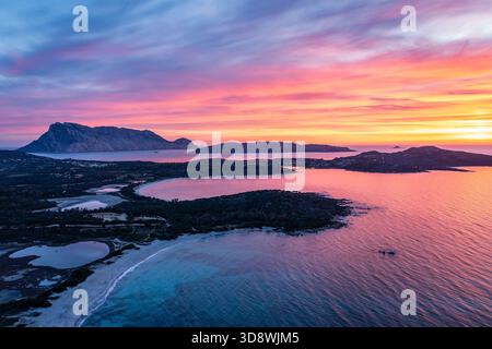 Ein atemberaubender Blick aus der Vogelperspektive auf eine Küstenlandschaft bei Sonnenuntergang, mit türkisfarbenem Wasser, rosa und orangefarbenem Himmel, Sardinien, Italien Stockfoto