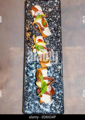 Blick von oben auf elegante Gourmet-Vorspeisen (Tapas/Pintxos) mit Sardellen, Weichkäse, Gemüse und Mikrogemüse auf Crackern, serviert auf A da Stockfoto