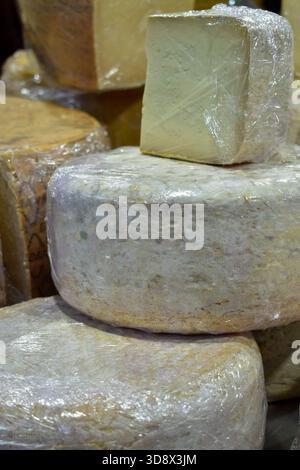 Vertikaler Nahstapel großer, runder, handgefertigter Käseräder, in Kunststoff gewickelt. Konzentriere dich auf die Struktur und Details der Rinde. Konzept des Gourmet Food mA Stockfoto