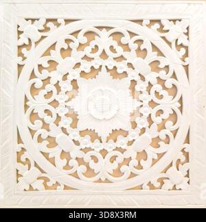 Quadratische weiße Holztafel mit komplizierten, floralen Mandalaschnitzereien auf neutralem Hintergrund. Ideal für Bohème, ethnische oder traditionelle Innenarchitektur der Stockfoto