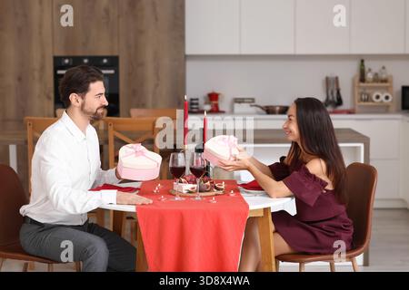 Liebevolles Paar tauscht Geschenke an einem Esstisch in der Küche aus. Valentinstag-Feier Stockfoto