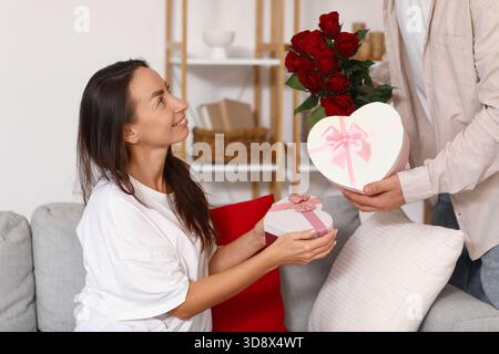 Liebevolles Paar, das zu Hause Geschenke und Blumen austauscht. Valentinstag-Feier Stockfoto