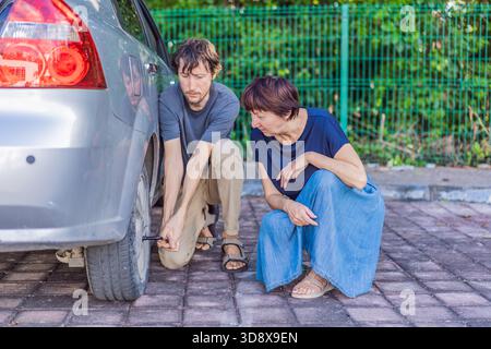 Junger Mann hilft einer älteren Frau, indem er das Autorad wechselt, während sie in der Nähe sitzt, und zeigt Unterstützung, Freundlichkeit und echte Pannenhilfe. Familie Stockfoto