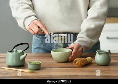 Frau, die Matcha-Tee am Holztisch in der Küche zubereitet Stockfoto