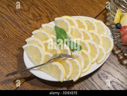 Viele der halben Zitronenscheiben, dekoriert mit Minzblättern auf weißem Teller, mit Gabel auf Holztisch. Stockfoto