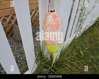 Alte und verwitterte Hummer-Angelboje, die am weißen Zaun hängt Stockfoto