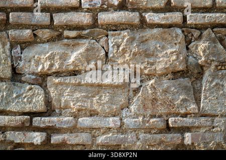 Eine Wand aus Stein mit rauer Textur. Die Wand besteht aus Ziegeln und hat eine graue Farbe Stockfoto