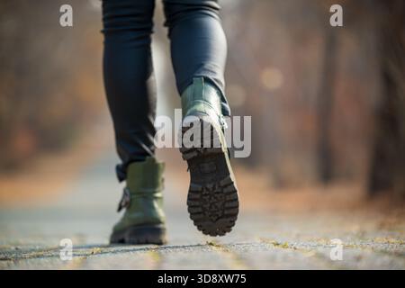 Eine Frau mit grünen Stiefeln geht auf einem Weg. Die Stiefel sind schwarz und grün und die Hose der Frau schwarz. Das Bild hat eine ruhige und friedliche Atmosphäre Stockfoto