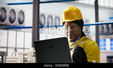 Frau führt routinemäßige Inspektionen in Solaranlagen der Industrie 4,0 mit Laptop durch. Ingenieurin für intelligente Fotovoltaik-Werkstests und Überprüfung von Systemkennzahlen mit einem Notebook Stockfoto