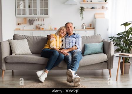 Seniorenpaar genießt eine gute gemeinsame Zeit auf einem gemütlichen Sofa in einem hellen Wohnzimmer Stockfoto