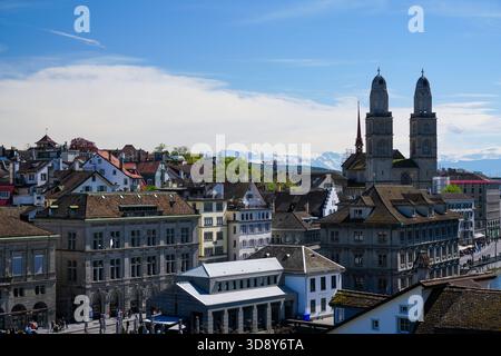 Skyline der Zürcher Altstadt mit Zwillingstürmen der Grossmünster-Kirche und schneebedeckten Schweizer Alpen unter blauem Frühlingshimmel. Stockfoto