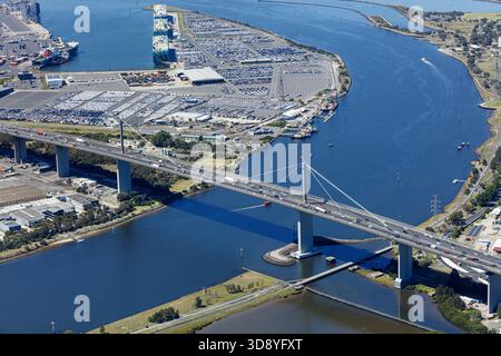 Aus der Vogelperspektive auf die Bolte Bridge, die sich über den Yarra River erstreckt, mit Schiffen, die am Hafen angedockt sind und Autos auf riesigen Grundstücken, Melbourne, Victoria, Au, geparkt haben Stockfoto