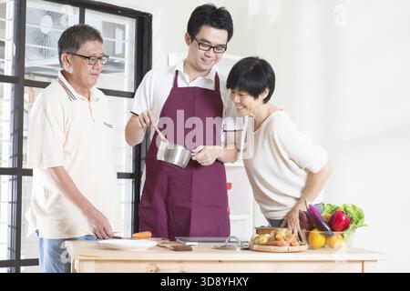 Asiatischer erwachsener Sohn, der in der Küche Essen für seine Senioreneltern zubereitet. Familienleben zu Hause Stockfoto