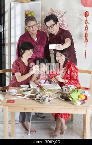 Glückliches chinesisches Neujahr, Selfie beim Wiedersehen-Dinner. Glückliche asiatisch-chinesische Familie mehrerer Generationen mit rotem Cheongsam-Essen zu Hause Stockfoto