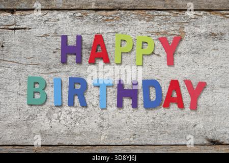 Die bunten Worte HAPPY BIRTHDAY aus Holzbuchstaben auf altem Holzbrett Stockfoto