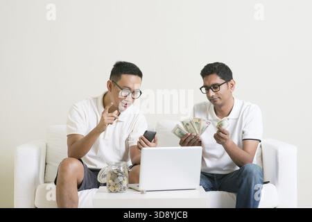 Asiatische Männer, die von zu Hause aus arbeiten. Junge Leute zählen mit ihrem Partner Bargeld und verdienen Geld mit ihrem erfolgreichen Online-Geschäft Stockfoto