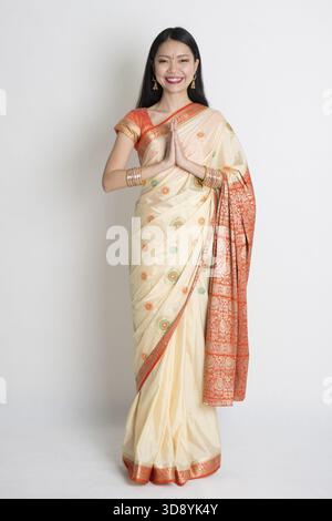 Indische Asiatin in einem Gruß Pose, traditionellen Sari Kostüm, auf einfarbigen Hintergrund stehen in voller Länge Stockfoto