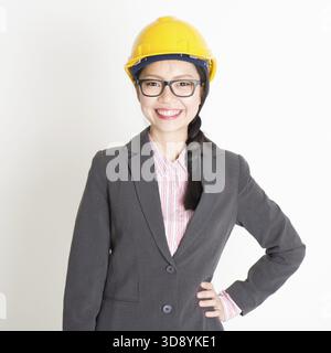 Porträt einer asiatischen Ingenieurin mit einem Helm, der lächelnd und in die Kamera blickt, auf glattem Hintergrund Stockfoto