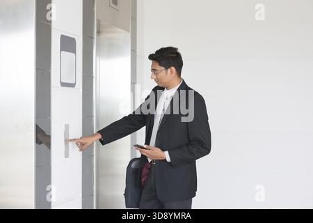 Asiatisch-indischer Geschäftsmann, der auf den Fahrstuhlknopf drückt, wartete Tür offen, um in den Aufzug zu gelangen Stockfoto