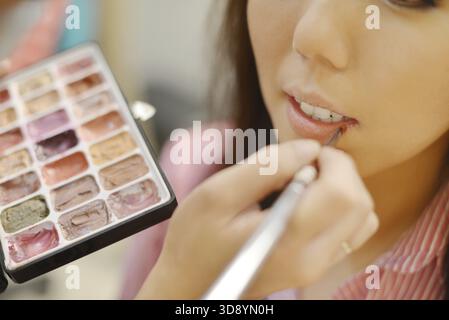 Junge, schöne asiatische Braut, die Hochzeit von Make-up-Künstlern schminkt. Konzentrieren Sie sich auf die Lippen Stockfoto