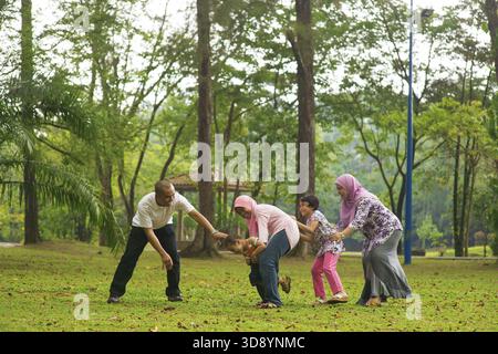 Muslimische Familie hat Spaß im grünen Outdoor Park. Schöne südostasiatische Familie, die zusammen spielt Stockfoto