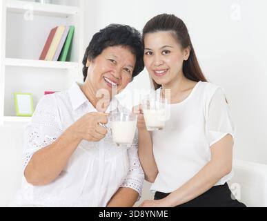 Trinkmilch. Glückliche asiatische Familie, die zu Hause Milch trinkt. Schöne ältere Mutter und Erwachsene Tochter, Gesundheitskonzept Stockfoto
