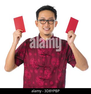 Glücklicher südostasiatischer chinesischer Mann in Cheongsam-Händen, der zwei rote Pakete / ang Pow hält, isoliert auf weißem Hintergrund Stockfoto