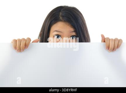 Schock asiatische Frau, die große Augen öffnet, sich hinter einer weißen Karte versteckt und den Mund bedeckt Stockfoto