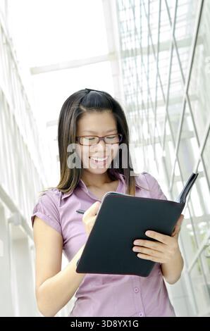 Junge asiatische Führungskraft schreibt auf Tagebuch, Büroumgebung Stockfoto
