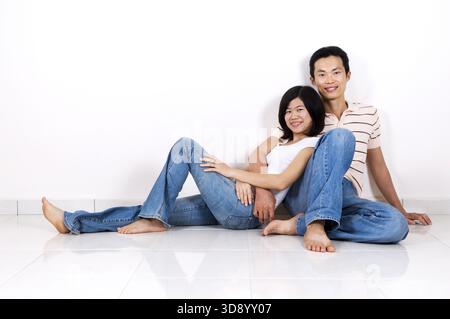 Junge asiatische Erwachsene Paare sitzen zusammen auf Fliesenboden zu Hause lächelnd Stockfoto