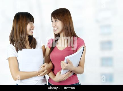 Zwei glückliche asiatische Schüler mit Büchern, die auf dem Schulgelände sprechen Stockfoto