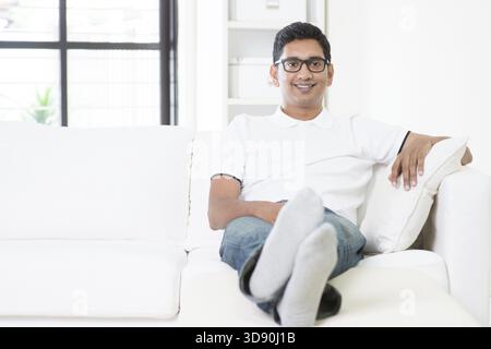 Gutaussehender indischer Mann, der auf dem Sofa sitzt und drinnen lächelt. Lebensstil eines lässigen Mannes zu Hause Stockfoto