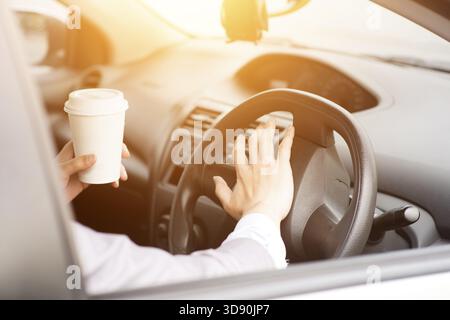 Konzeptfoto: Nahaufnahme der Hand beim Hupen der Lenkung während der Fahrt am Morgen, eine andere Hand hält die Kaffeetasse Stockfoto
