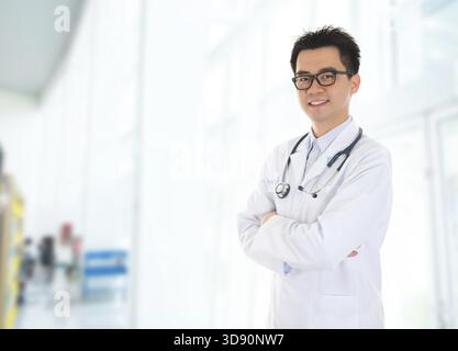 Asiatischer männlicher Arzt mit selbstbewusstem Lächeln, der im Krankenhausgebäude steht Stockfoto