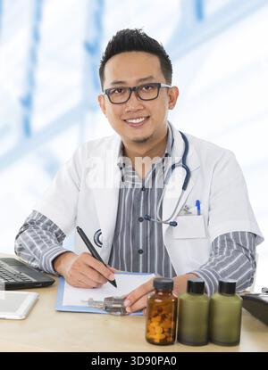 Junger südostasiatischer Arzt, der auf seinem Schreibtisch im Krankenhauszimmer arbeitet Stockfoto