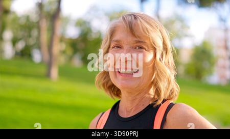 Glückliche lächelnde Seniorin mit Sportoutfit, die draußen genießt Stockfoto